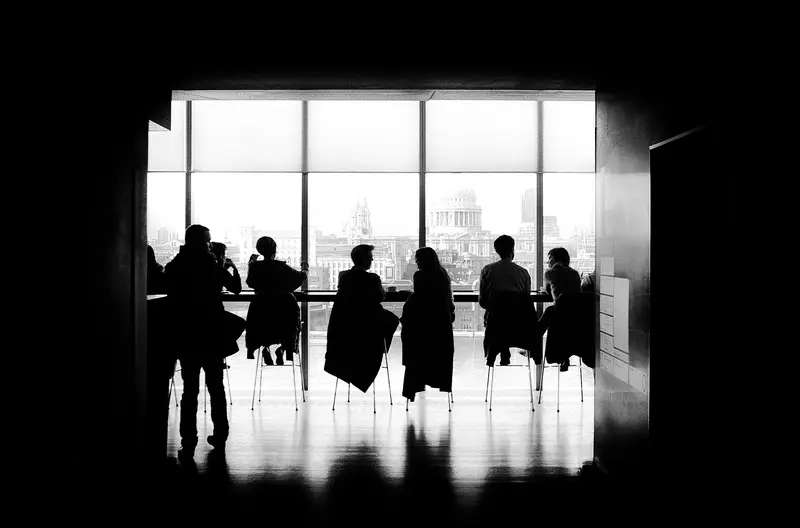 Silhouettes of a team in discussion around a long table by a window