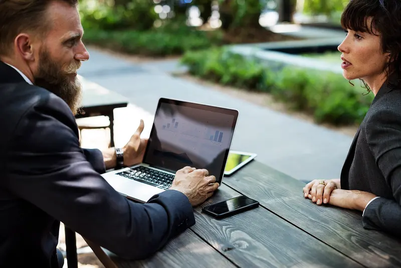 Two professionals discussing strategy at an outdoor table with a laptop
